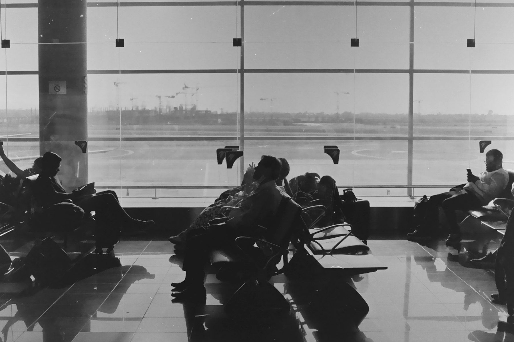 Sala de espera de un aeropuerto: personas sentadas frente al ventanal que da a la pista